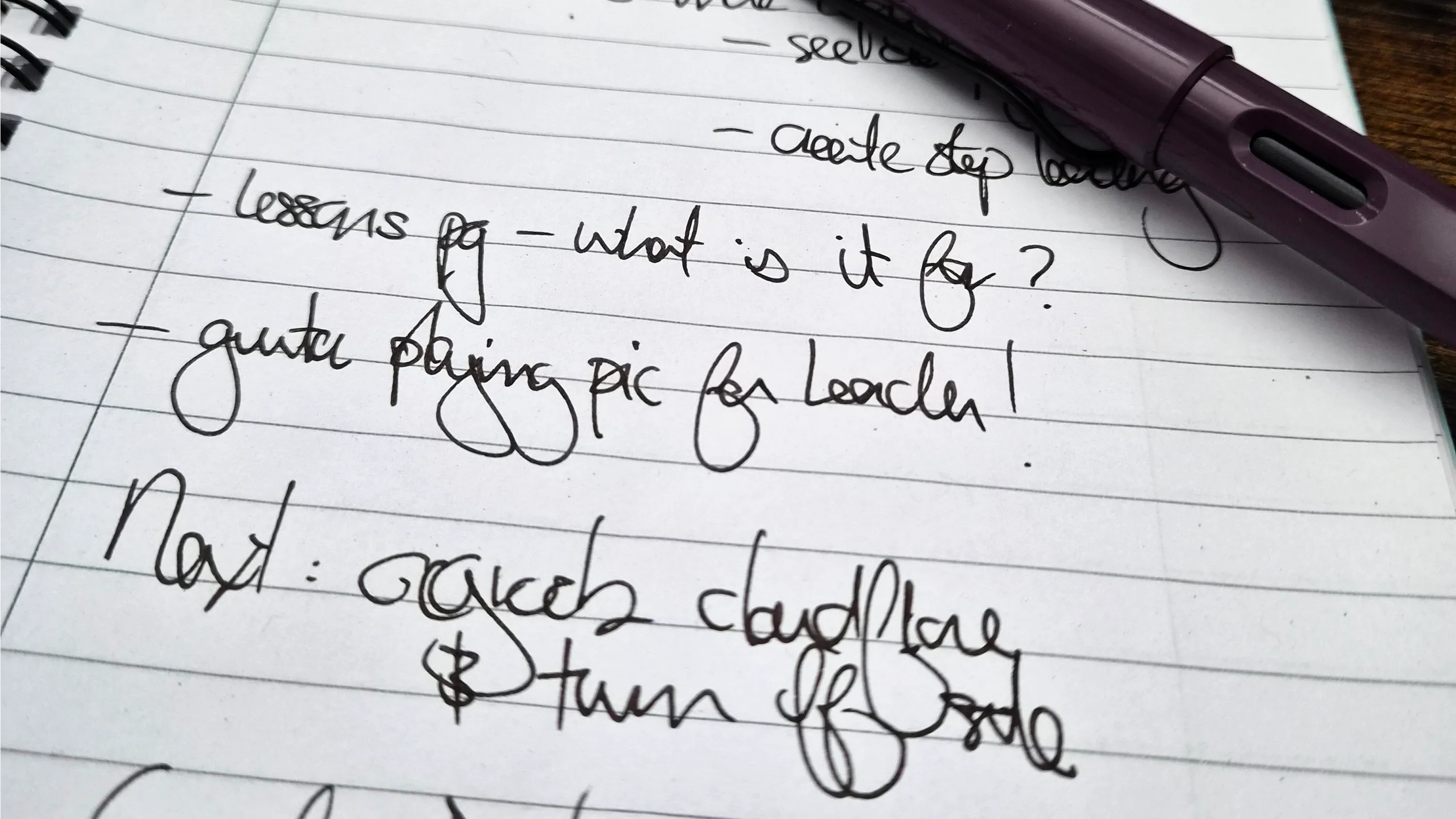 A spiral notebook on a dark desk, open to a handwritten planning list for this site, a fountain pen resting across the page.